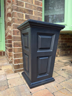 Black decorative planter against a brick wall