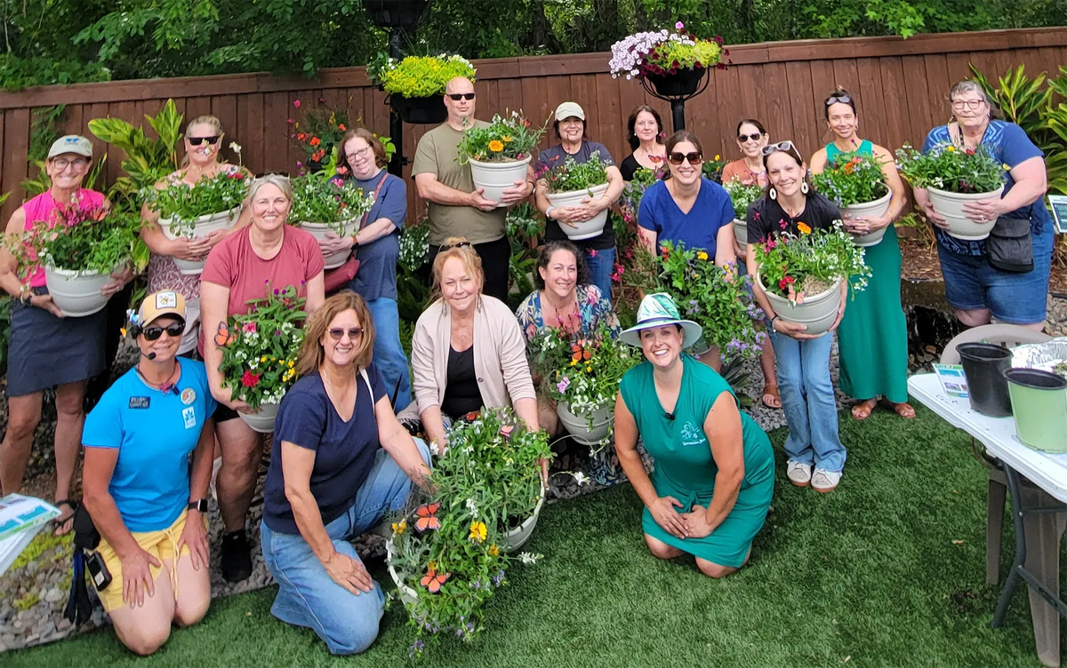 A group of people holding potted plants to showcase their creations from a class.