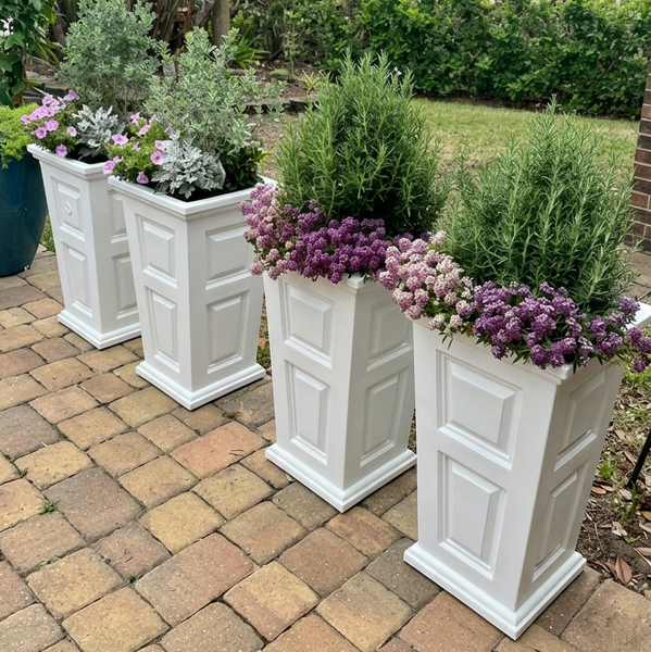 White planters with greenery and purple flowers on a brick patio